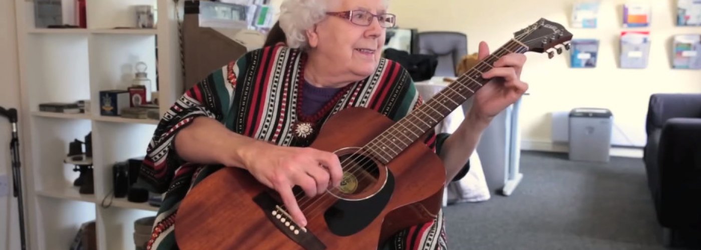 Grey haired woman playing a guitar